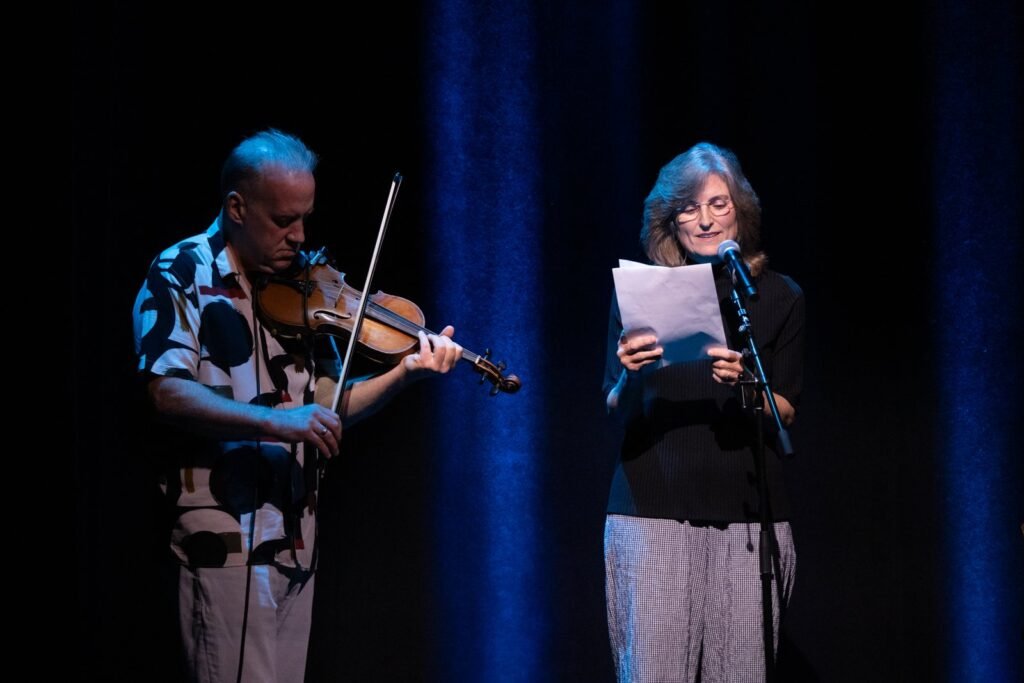 Christian Howes playing violin beside Francesca Bell as she reads poetry at Presidio Theatre in San Francisco